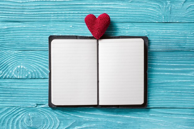 Blank notepad for copy space and vintage handmaded valentines day toy heart over light blue wooden background