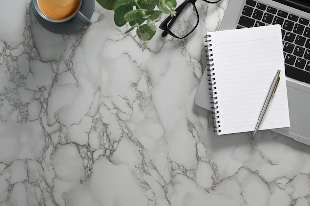 Blank notepad laptop eyeglasses and cup of coffee on marble table