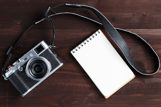 빈 메모장 페이지와 어두운 갈색 나무 테이블에 고전적인 스타일의 현대 카메라