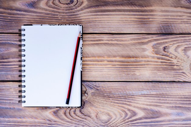 Blank notepad and pencil on wooden background.