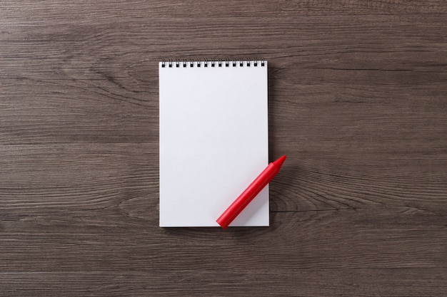 Blank notepad red crayon on dark wooden modern office table mock up top view