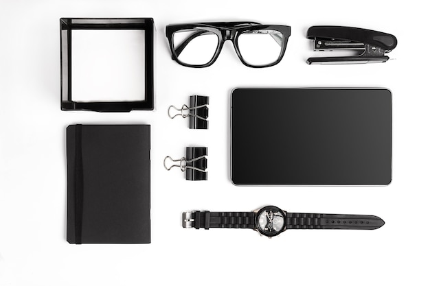 Blank notepad with clips, pens and glasses flat lay. Top view on set of black office supplies and spectacles on a white background