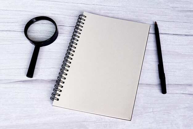 blank notepad with pen and magnifying glass on a white wooden table flat lay directly above copy space