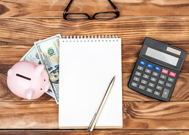 Blank notepad with piggy bank money and calculator on the table Top view