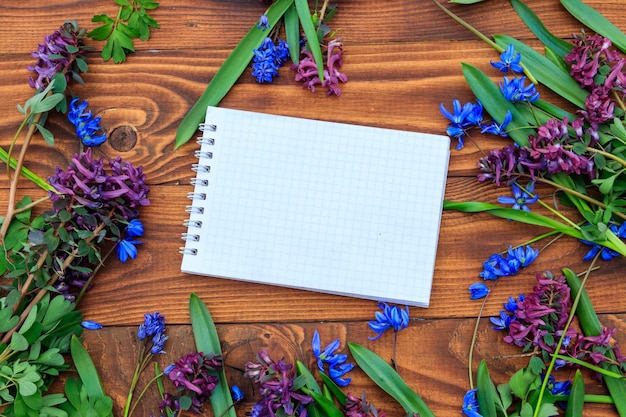 Blank notitieboek en boeket van paarse corydalisbloemen en blauwe scillabloemen op houten achtergrond