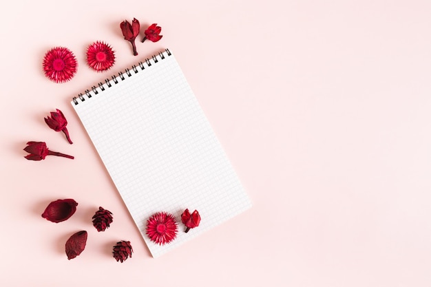 Blank notitieboek voor schrijven en droge rode bloemen op een roze achtergrond bovenaan