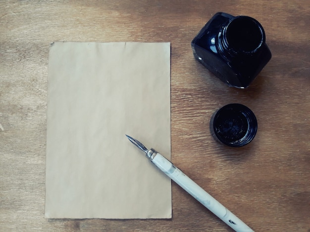 Blank old sheet of paper with a dip pen and an inkwell on a worn wooden background, retro style