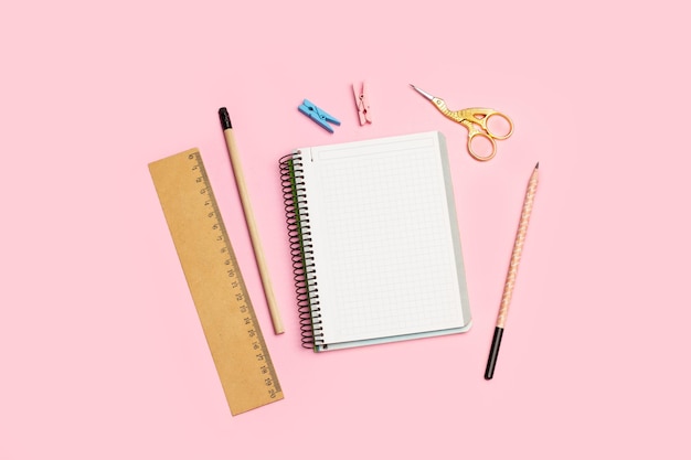 Blank open graph paper notebook two pencils a ruler and a stork scissors on a pink background