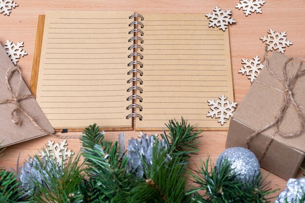 空白の開いたノート、日記、手作りの箱に入ったギフト、モミの枝と木製の雪片、フラットレイ、上面図、コピースペース。ギフトリストのコンセプト。新年の計画のコンセプト。環境にやさしいスタイル。