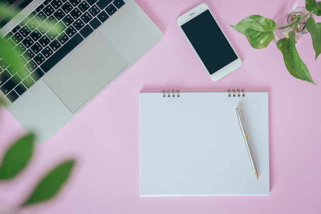 Blank opened notebook with laptop, smartphone on pink background. flat lay, top view