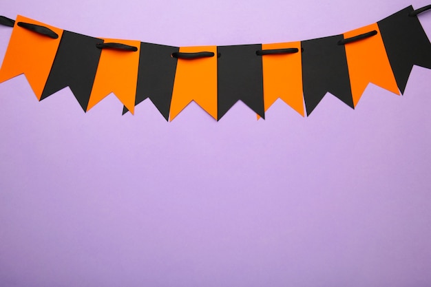 紫の背景にハロウィーンの装飾のための空白とオレンジ色のパーティーフラグ。上面図