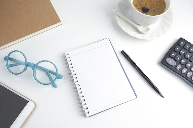 The blank page notebook on desktop with pen,coffee,laptop,book,calculator, glasses and mob