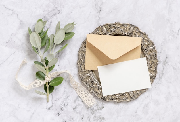 Photo blank paper card and envelope with eucalyptus branches on vintage plate on marble table top view. card mockup