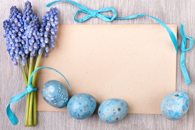 Blank paper card framed by blue ribbons, Easter eggs and grape hyacinth flowers, text space