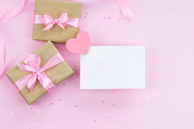 Фото Макет пустой бумажной карты на розовом фоне с подарками и конфетти в форме розового сердца