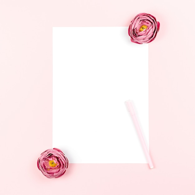 Photo blank paper card with pen and flowers frame on pastel background. top view