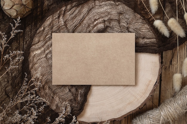 乾燥した植物が周りにある木製のテーブルの上の白紙のカード、上面図。招待カードテンプレートを使用した自由奔放に生きるモックアップシーン