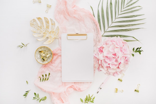 Пустой бумажный буфер обмена, розовые цветы гортензии и аксессуары на белой поверхности