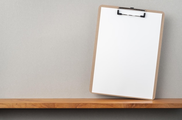 Photo blank paper in clipboard on shelf against gray wall