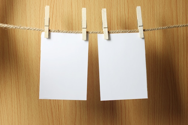 Blank paper hangs on the brown rope with Wooden paper clips on wood background.