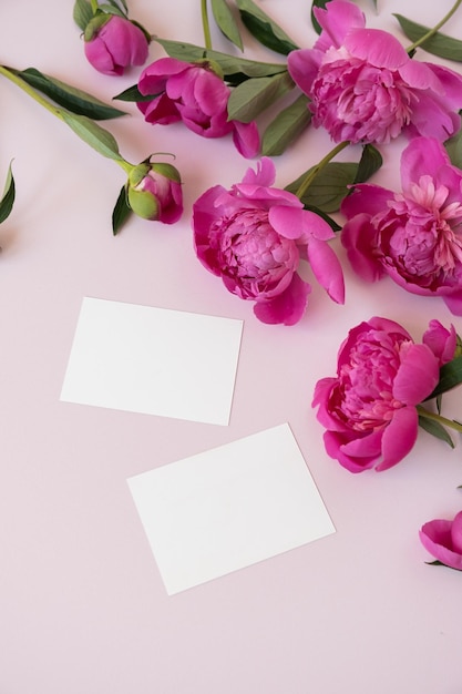 コピースペース付きの空白の紙の招待状カードニュートラルなパステル調のエレガントなピンクの背景にピンクの牡丹の花の花束フラットレイトップビュー最小限の花の組成