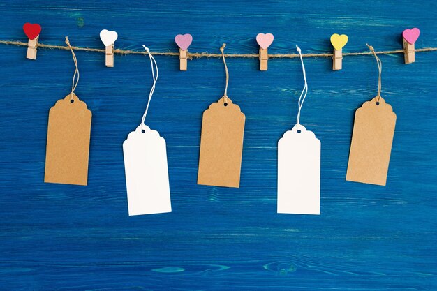 Photo blank paper price tags and wooden pins hanging on a rope on the blue wooden background