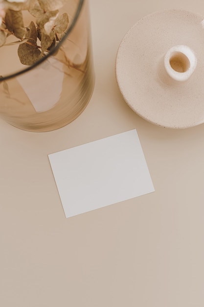 Blank paper sheet card with copy space, eucalyptus branch in glass vase on beige