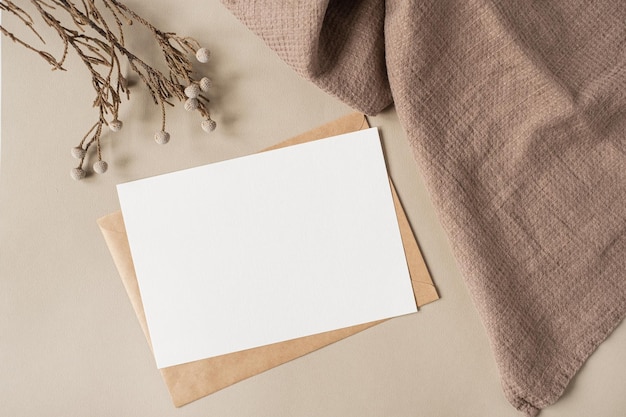 Scheda foglio di carta bianca con spazio per la copia del mockup e ramo floreale secco e panno di coperta su sfondo beige neutro modello di invito a nozze estetico minimale vista dall'alto piatta