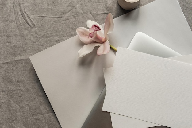 モックアップコピースペースラップトップコンピューターピンクの花のキャンドルと中立的なリネン布の背景と空白の紙のシートカード最小限の美的ビジネスブランドの結婚式の招待状のテンプレートフラットレイトップビュー