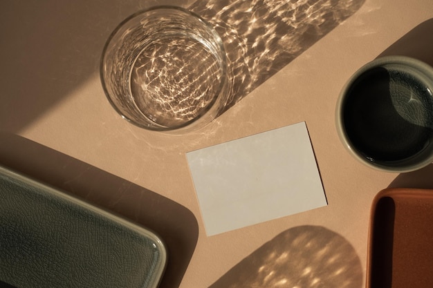 モックアップコピースペースが付いている空白の紙シートカード最小限の贅沢な美的ビジネスブランドテンプレート日光の影が付いているガラスニュートラルな桃色の背景にセラミックプレートフラットレイトップビュー