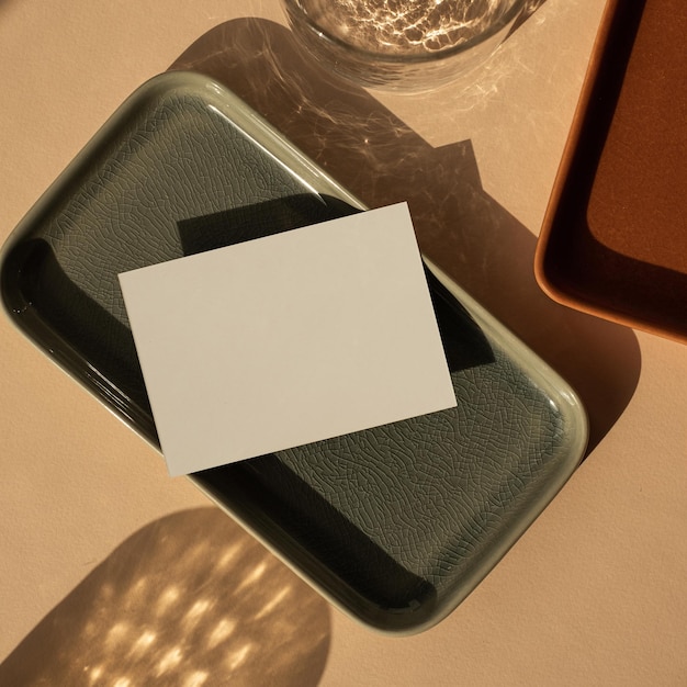 blank paper sheet card with mockup copy space on neutral peachy background aesthetic bohemian business brand template ceramic plates and glass with sparkling sunlight shadow reflections