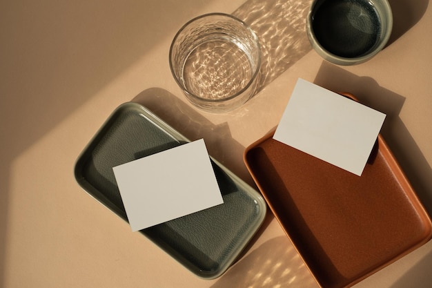 Foto scheda di foglio di carta bianca con spazio per la copia del mockup su sfondo color pesca neutro modello di marchio aziendale bohémien estetico piatti in ceramica e vetro con riflessi scintillanti dell'ombra della luce solare