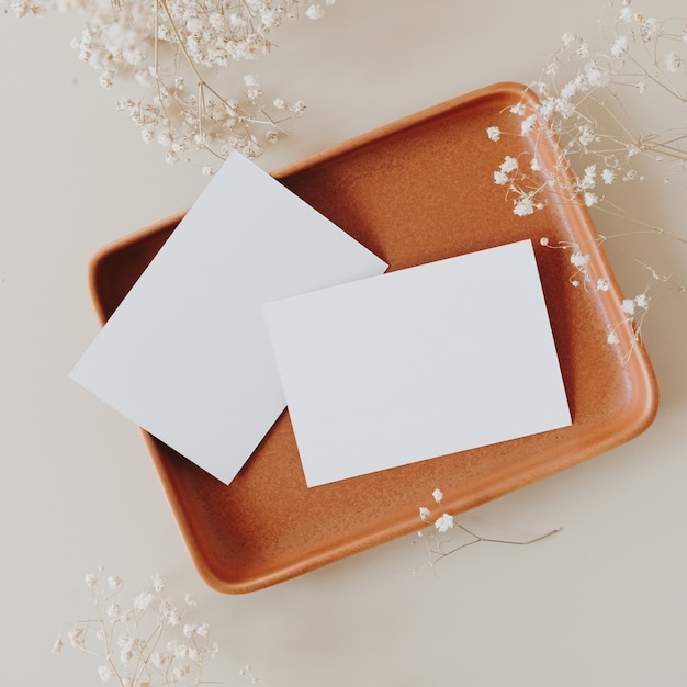 Blank paper sheet cards with copy space and gypsophila flowers bouquet on neutral beige. Flat lay, top view.