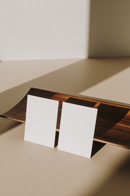 Blank paper sheet cards with copy space and wooden tray with sunlight shadow on beige