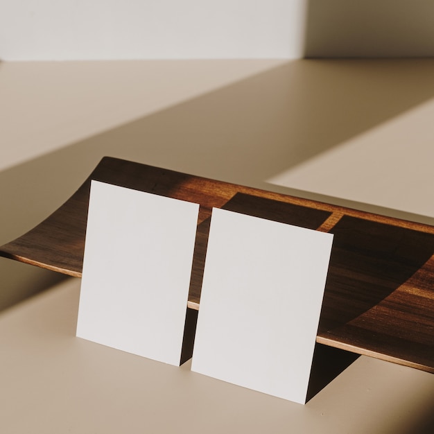 Blank paper sheet cards with wooden tray with sunlight shadow on beige background. Minimal business brand template