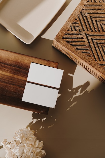 Blank paper sheet cards, wooden tray, casket and dry flowers with sunlight shadows on beige