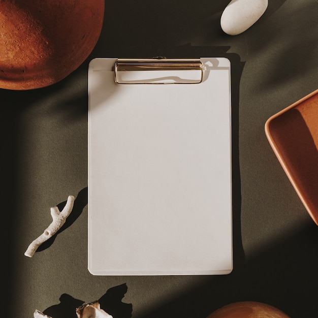 Blank paper sheet clipboard pad in sunlight shadows on deep green