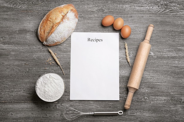 Foto foglio di carta bianco e ingredienti per cucinare il pane su fondo in legno