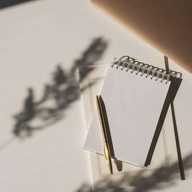 Photo blank paper sheet notebook with copy space flower sunlight shadows and laptop computer on white background aesthetic luxury minimalist workspace flat lay top view