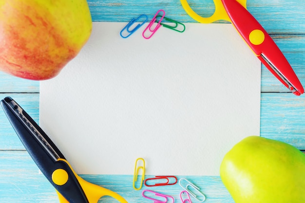 Blank paper sheet, two apples and scissors on blue background, top view