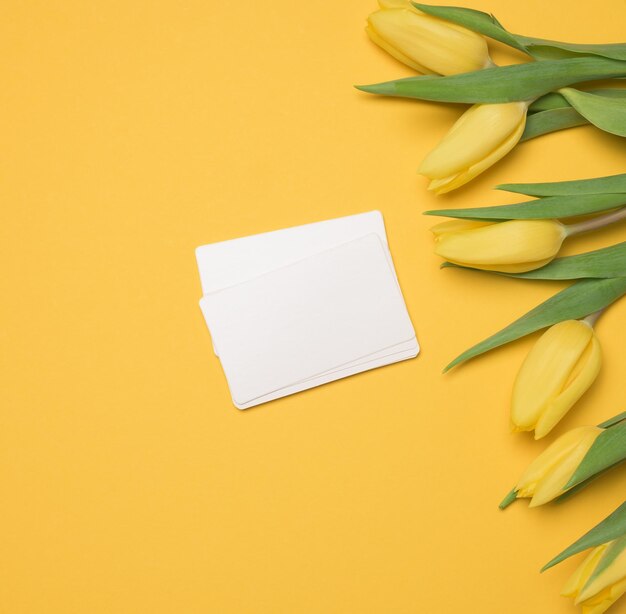 Foto un biglietto da visita bianco di carta bianca e un bouquet di tulipani gialli su uno sfondo giallo