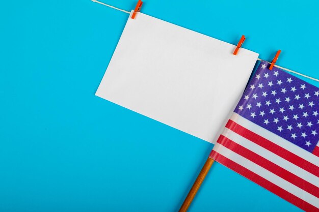 Photo blank paper with copy space hanging on clothesline besides usa flag on blue background. patriotism, symbol and identity.