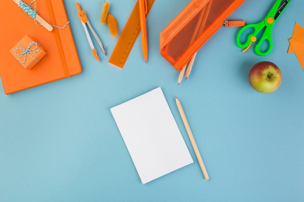 Blank paper with pen school or office workspace with orange supplies on blue background flat lay hig...