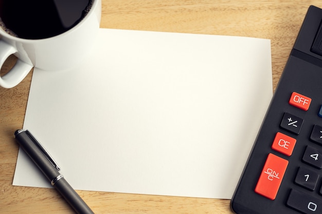 Blank paper on wooden desk table with cup of coffee and calculator. Mock up template. Economy, financial or business concept