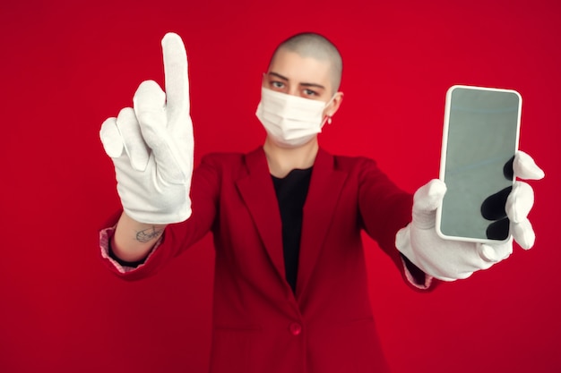 Blank phone's screen. Portrait of young caucasian bald woman isolated on red studio wall.