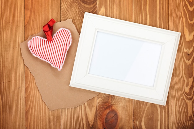 Blank photo frame and red Valentine's day heart toy. On wooden background