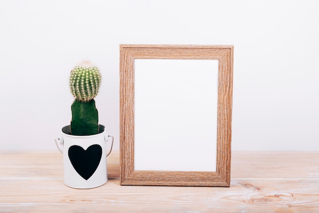 Blank photo frame and succulent plant with heartshape on pot over wooden table