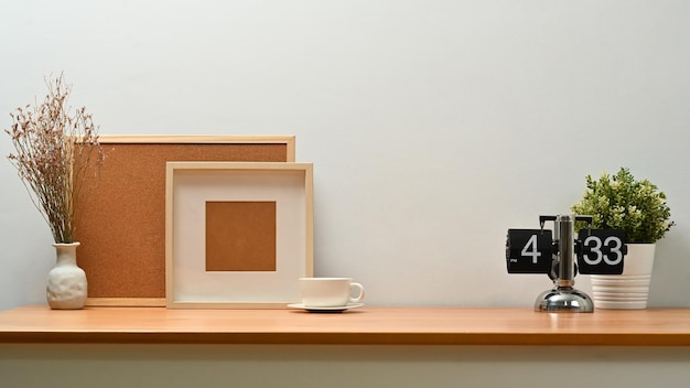 Пустая рамка для фотографий, петушиная доска, кофейная чашка и растение в горшке на деревянном столе