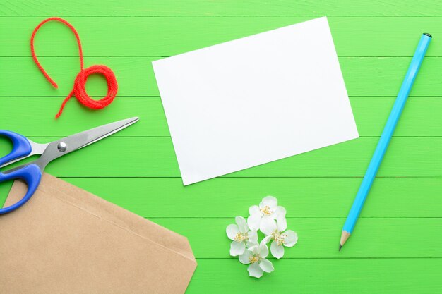 A blank piece of paper with an envelope on green wooden background