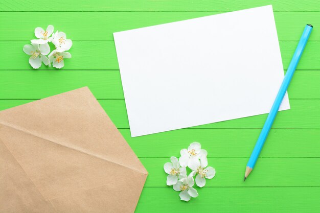 Photo a blank piece of paper with an envelope on green wooden background